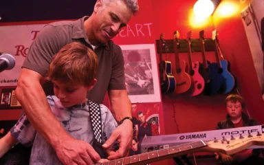 A teacher instructs a student on the proper way to hold a guitar.